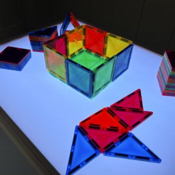 Mesa de luz Montessori con sillas con juguetes sobre una luz celeste